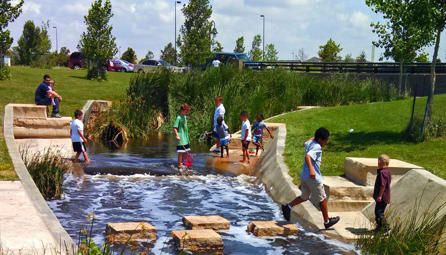 Children play with nets in a channeled river at a water access point.