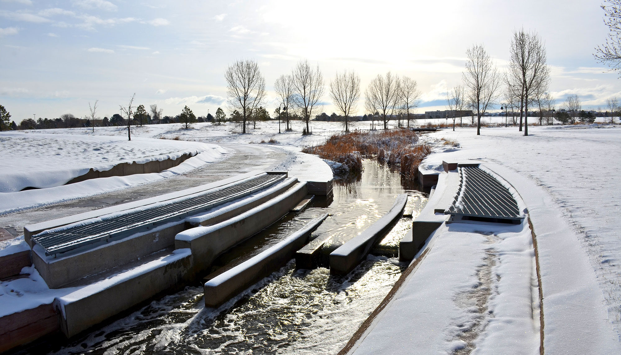 A sculptural concrete form shapes a rivers flow within a snowy field.