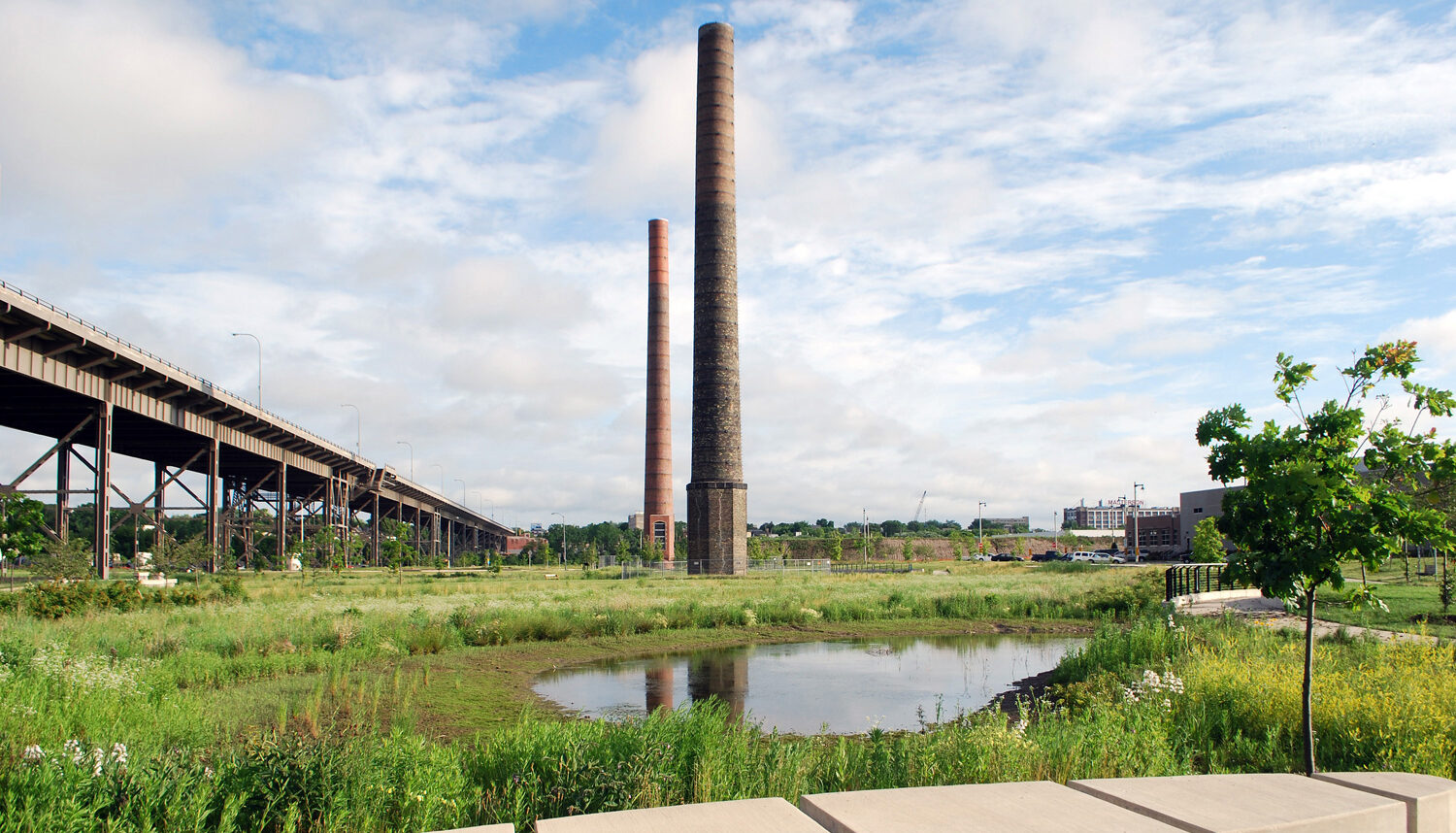 A natural-looking field with a small pond reflects two large smokestacks.