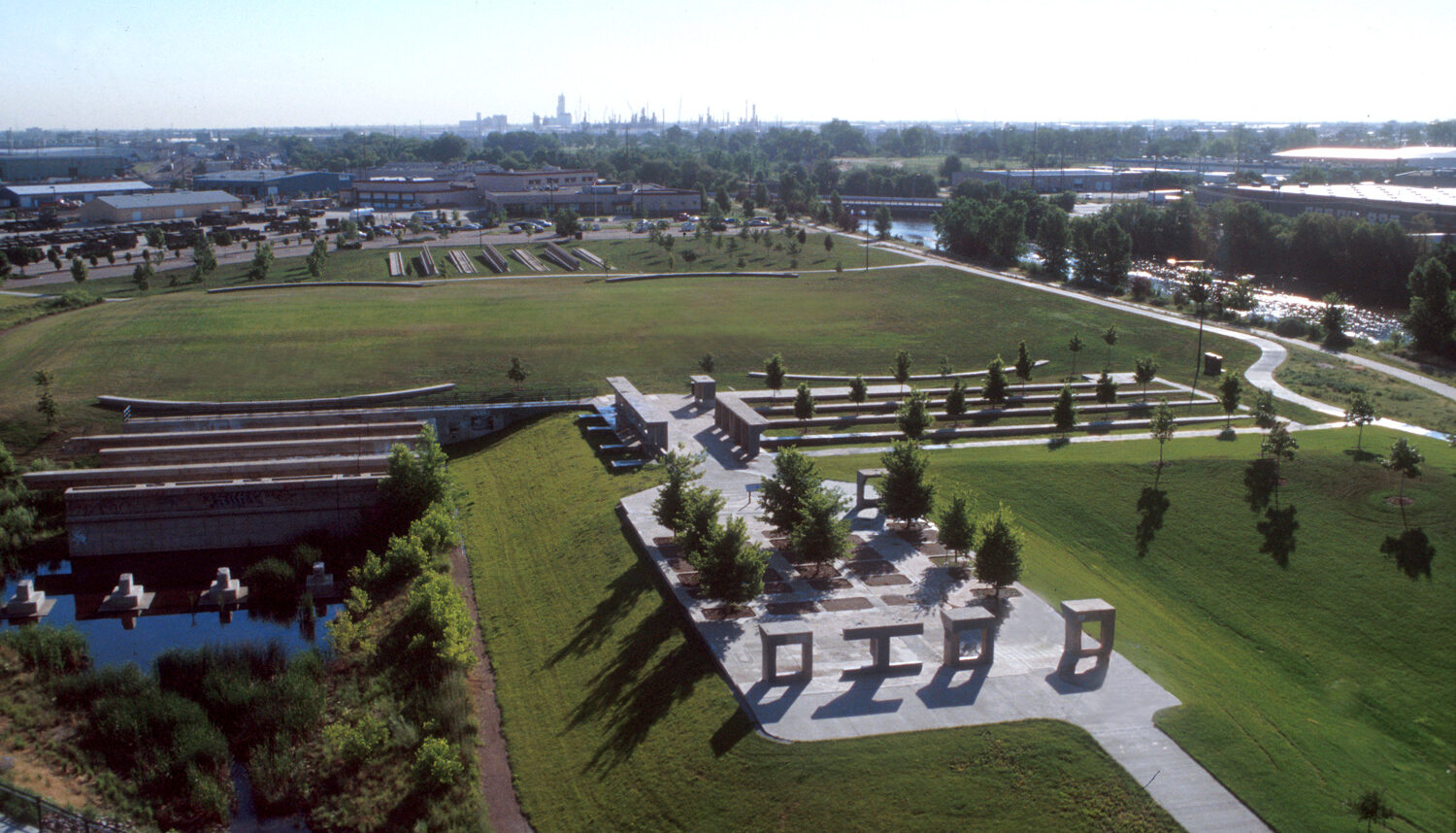 An aerial of the site shows large fields of turf grass with concrete pads, pathways, and old industrial forms positioned like sculptures.
