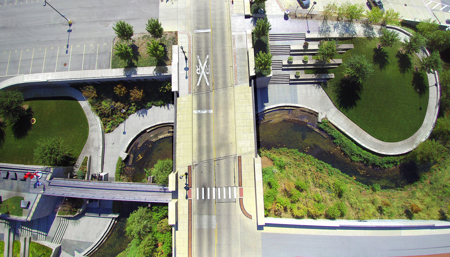 Aerial view of the Boneyard Creek from a drone shows the pedestrian bridge connection to the road, with the creek snaking underneath the vehicular bridge.