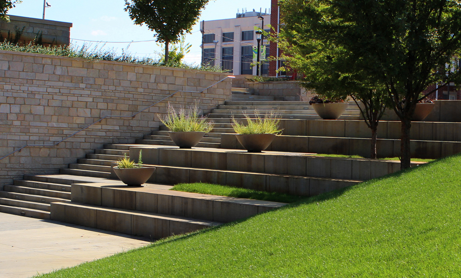 Terraces with large planters and steps lead visitors to the creek along a stone bridge abutment