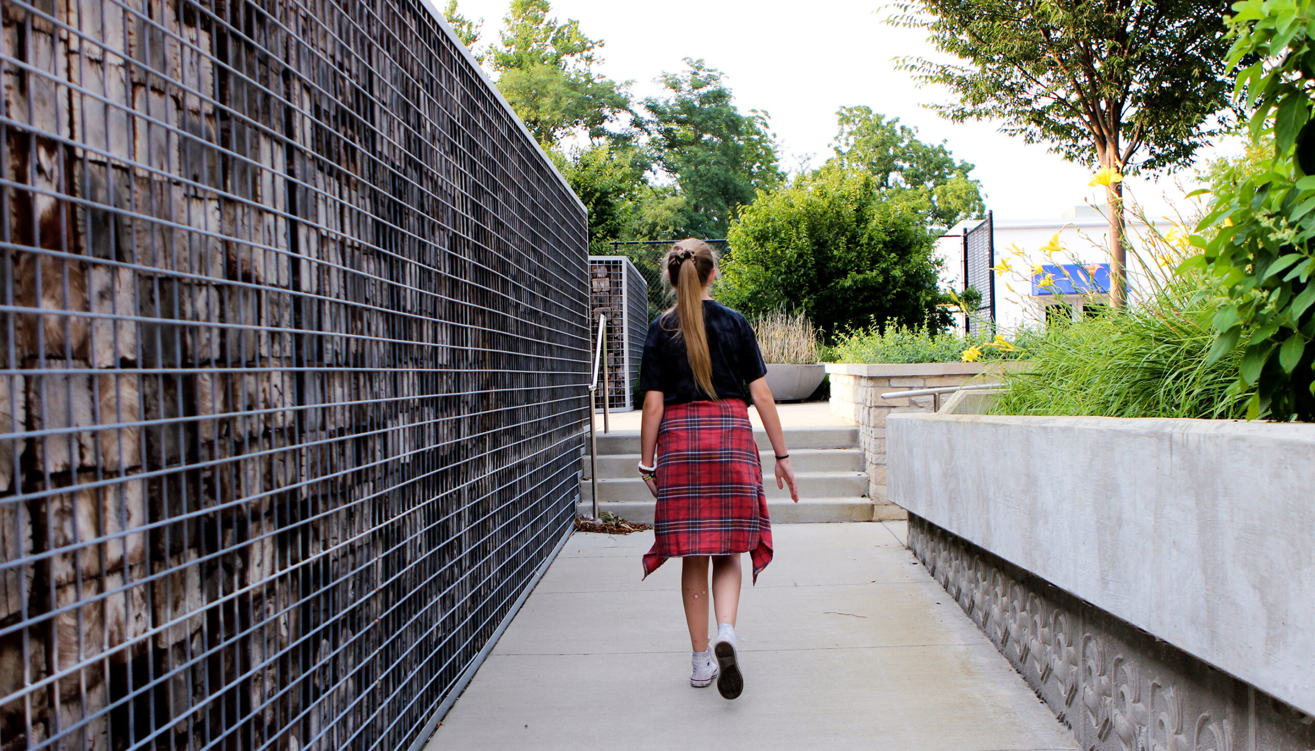 A young girl walks past a gabion wall filled with recycled wood trusses from the project area.