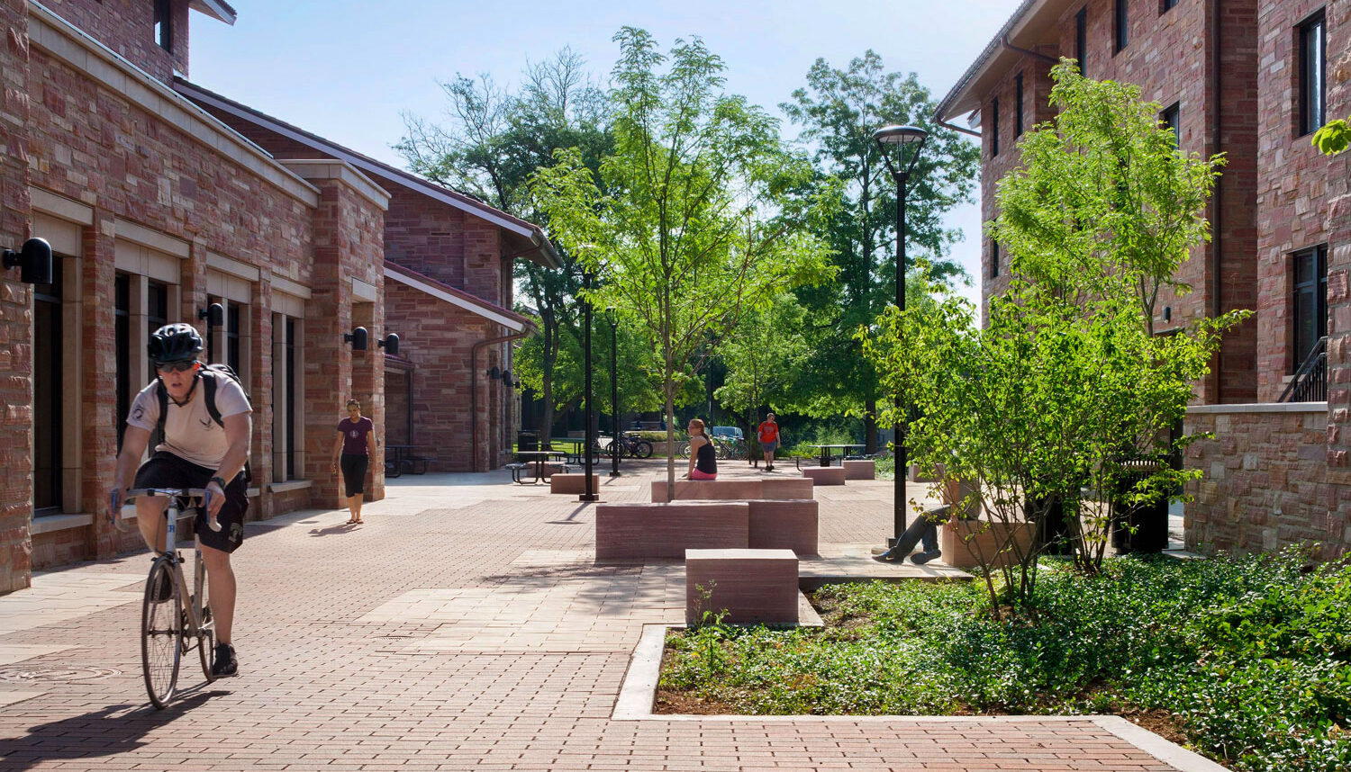 A photo shows students biking through a brick plaza with planting areas, and sandstone benches.