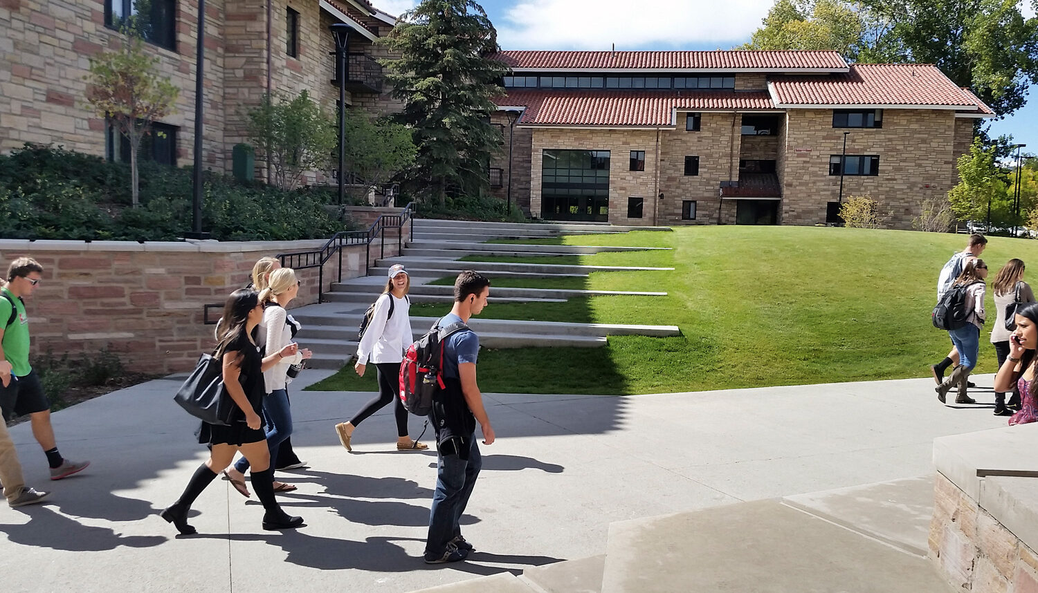 Students walk by a staircase that extends into the landform of the hill and disappears in the grass.