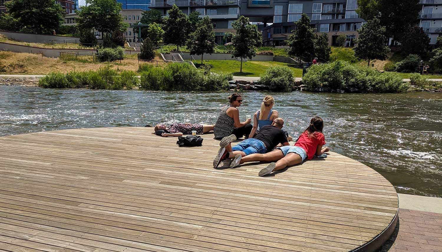 A small group of people lounge on a wooden platform along the edge of the river.