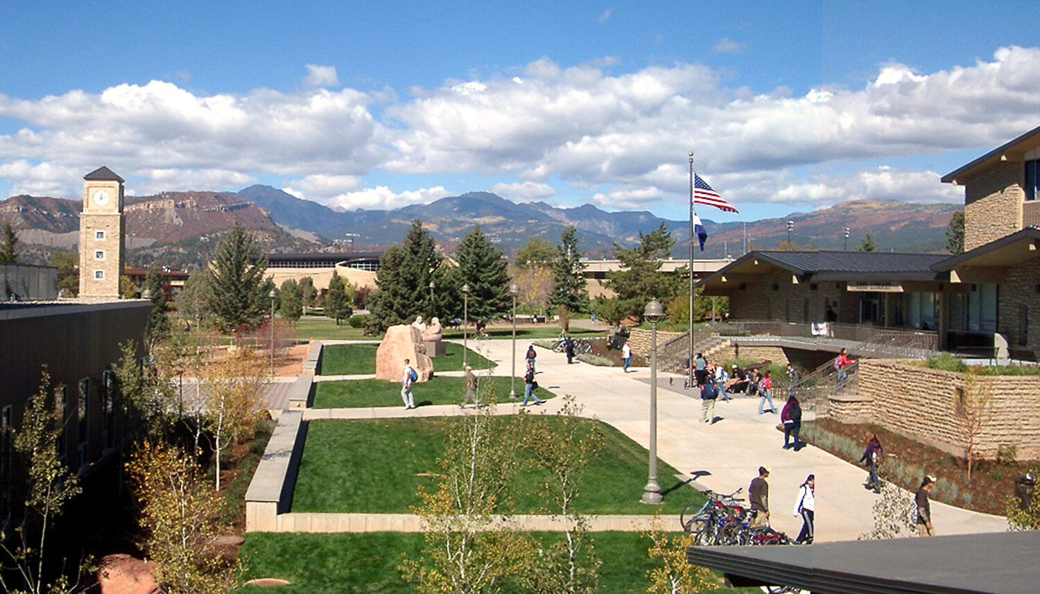 Photo shows students walking through a plaza with turf lawn areas and stone monuments.