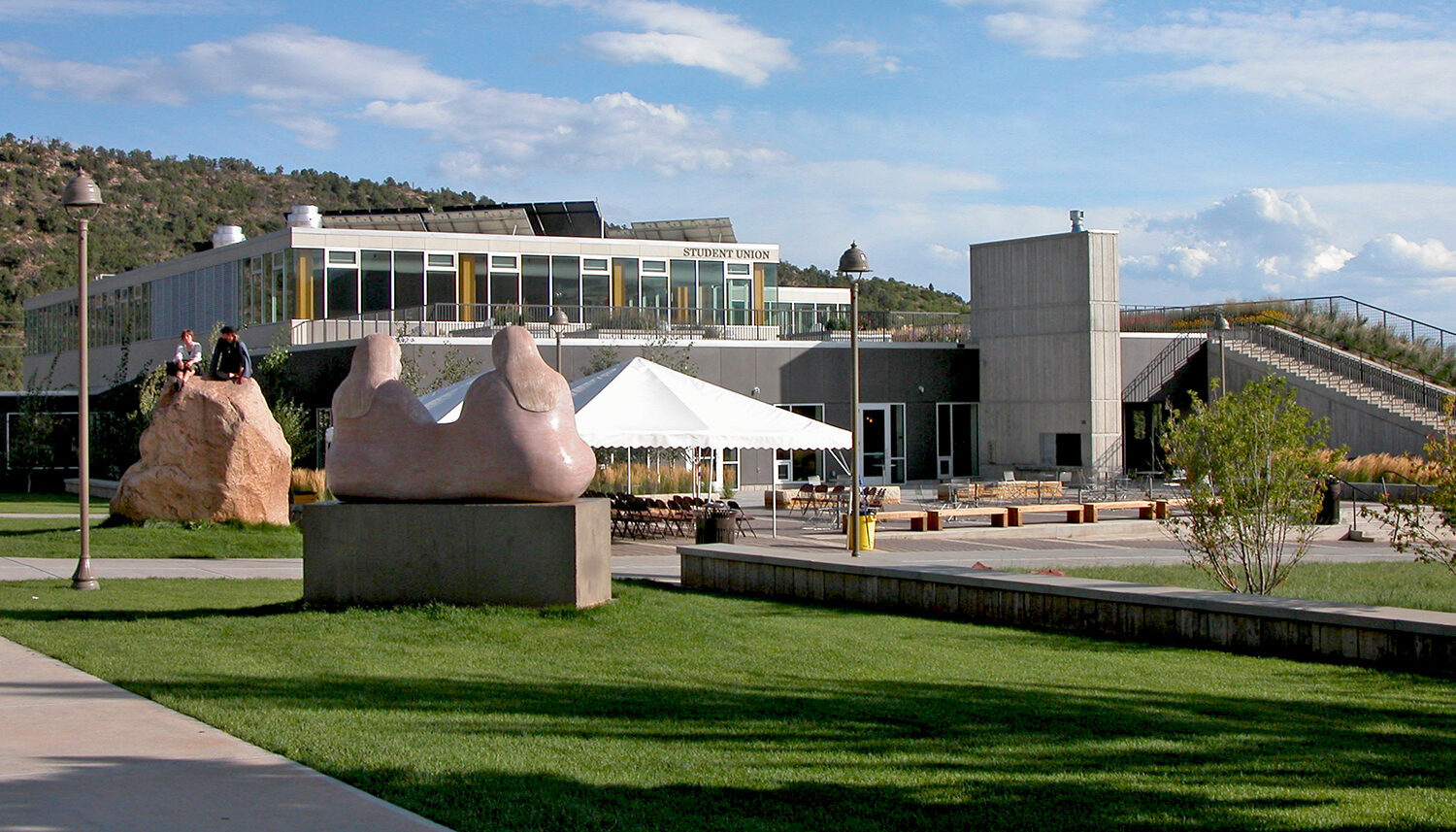 a photo shows students atop of stone monolith and stone monuments with a tent-covered plaza behind.