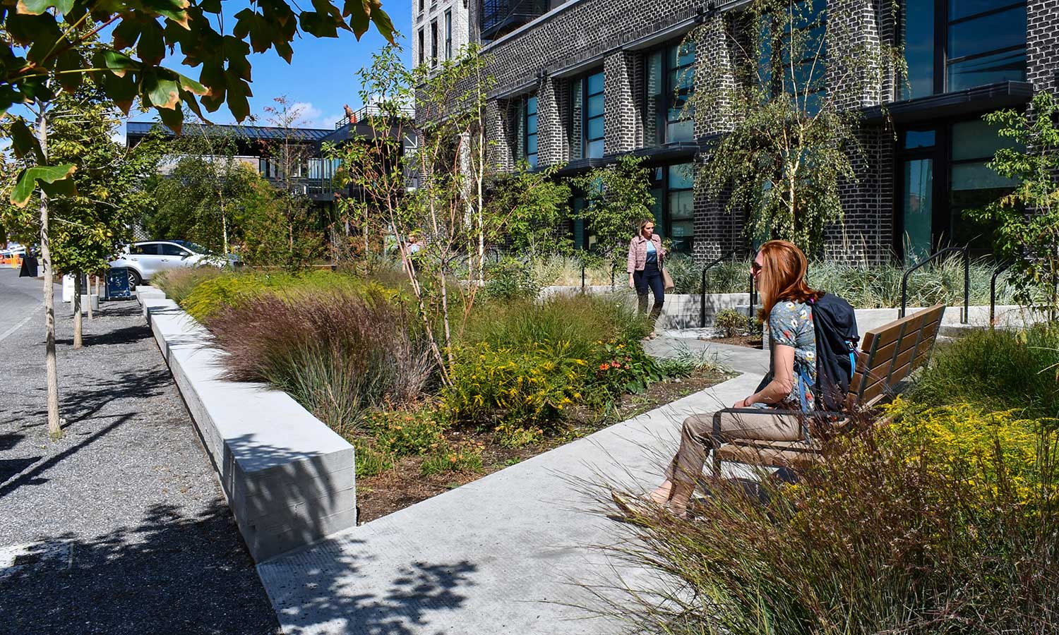A woman sits in the sunshine on a bench within the Post District gardens.