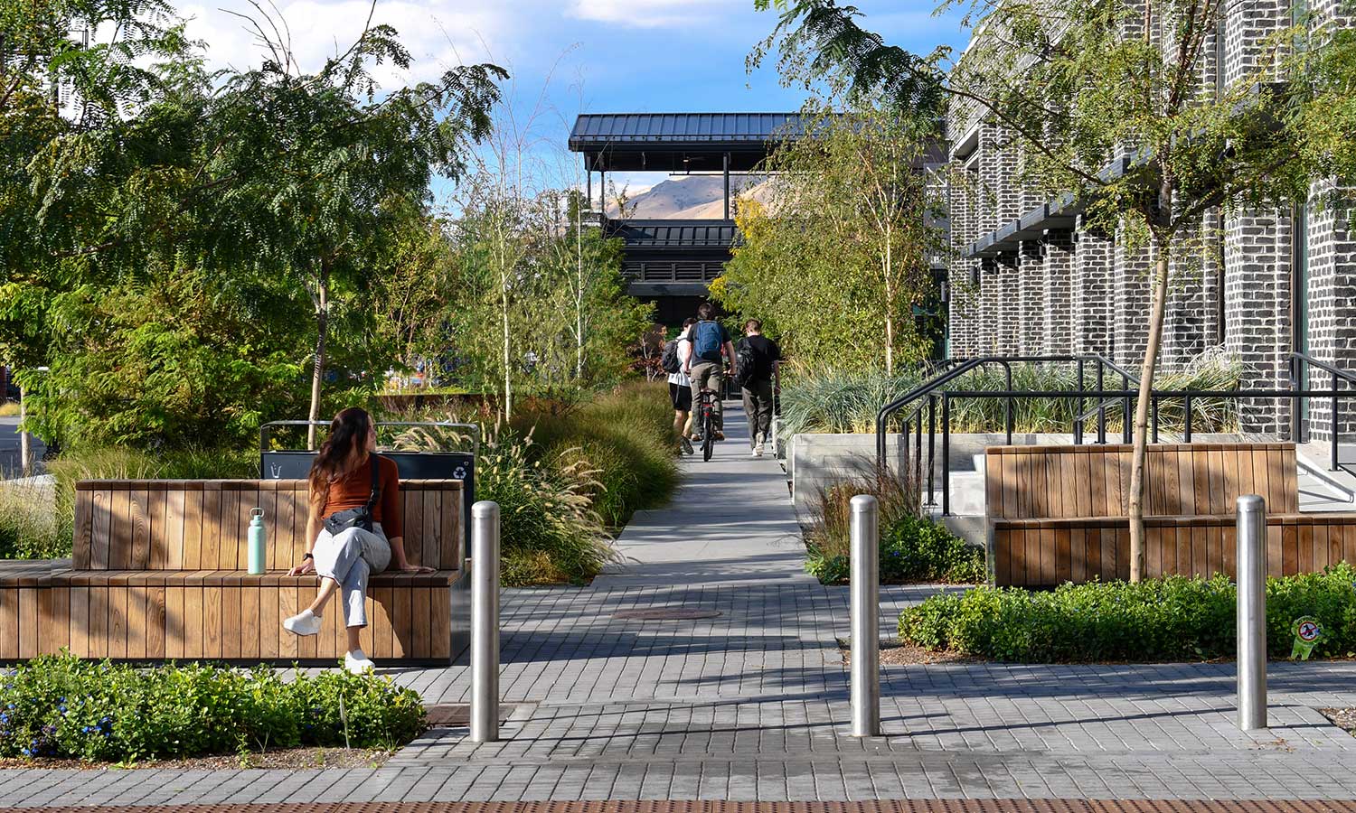 A woman sits on a bench while a group of boys walk along the garden path in the background.