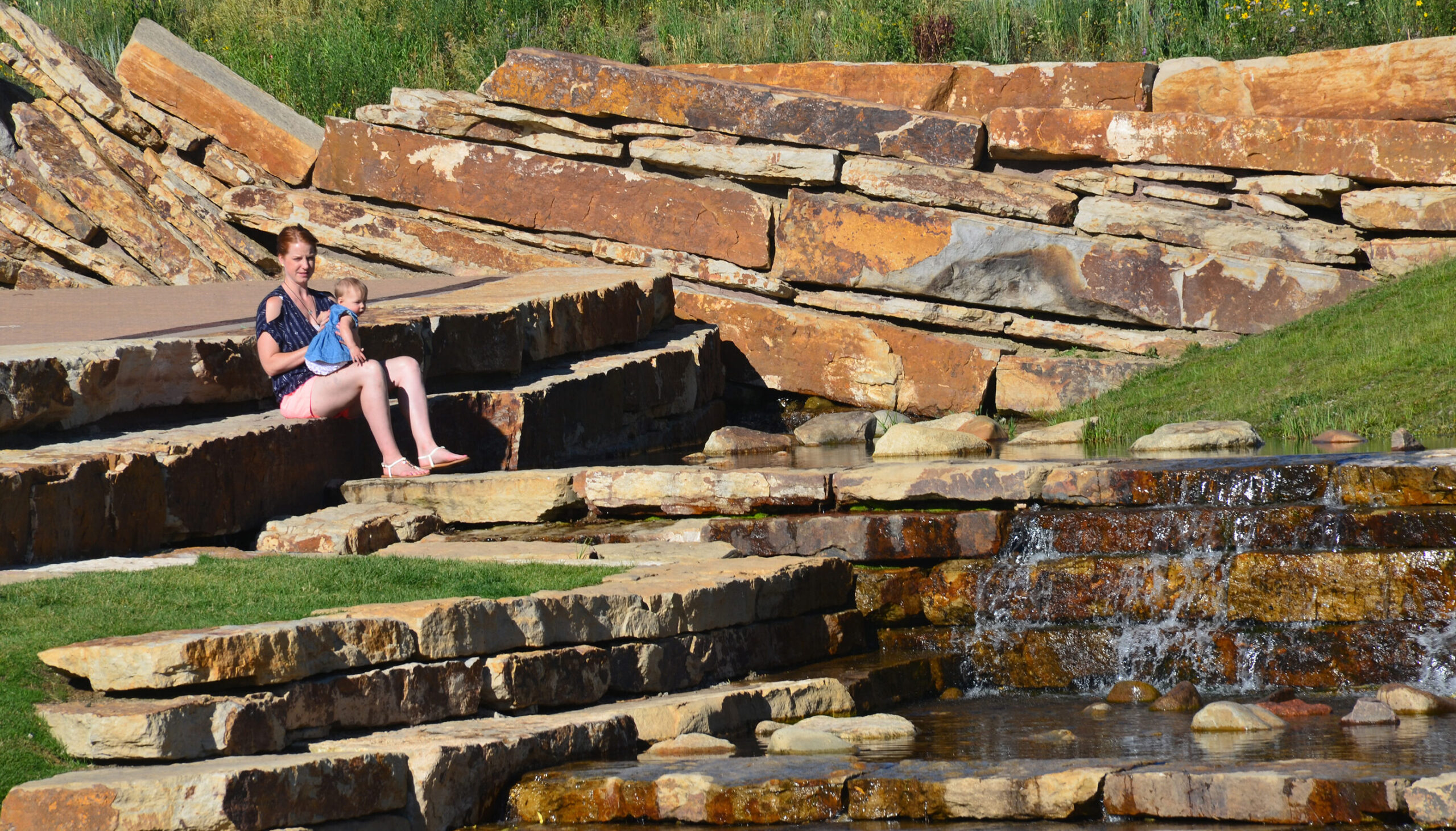 Mother and baby sit in the late afternoon sun on the massive stone water feature designed to mimic waterfall drops
