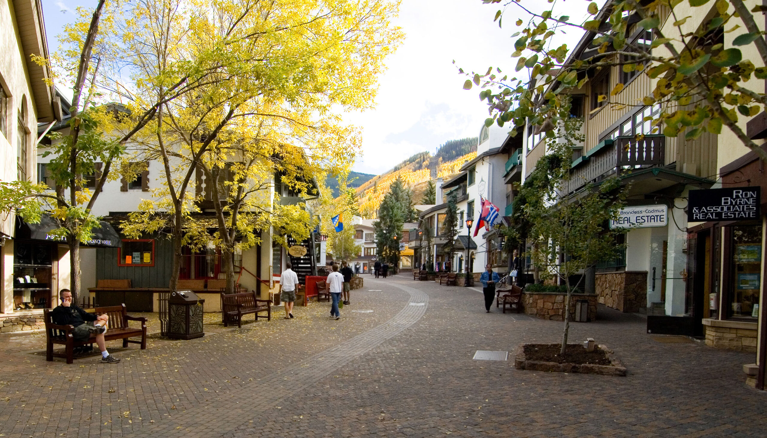 a cobblestone pedestrian street winds through Vail Village with yellow aspens speckling the mountains in the distance