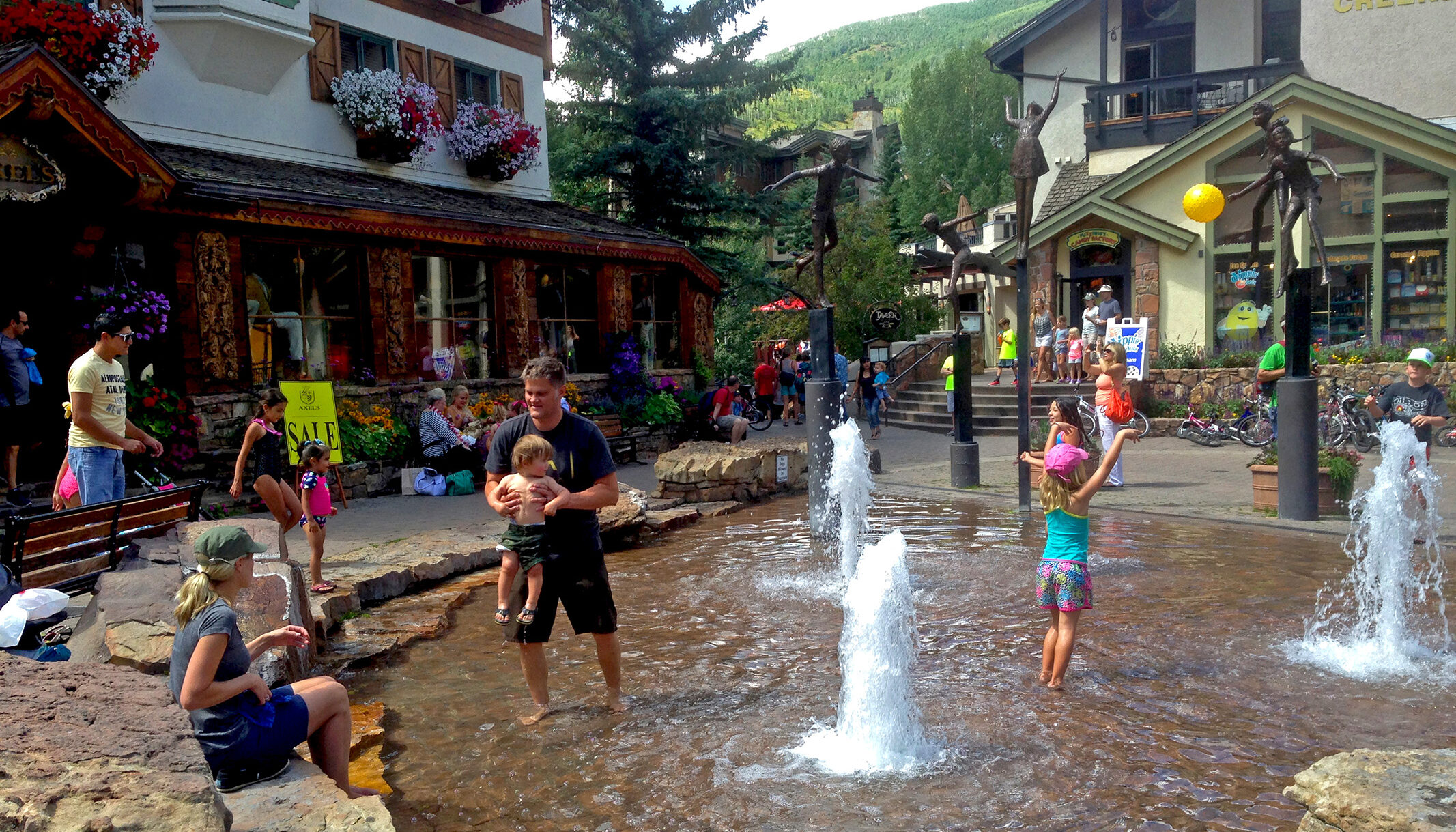 a girl plays in the water feature on a warm summer day and mimics the poses of the sculptures of children playing