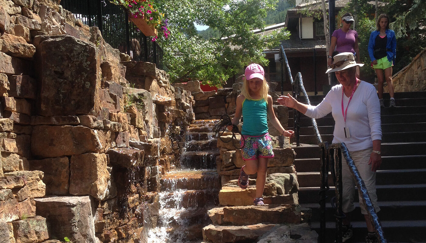 a girl and her grandmother play on the stepped stones of the water feature while the water trickles down the steps like a waterfall