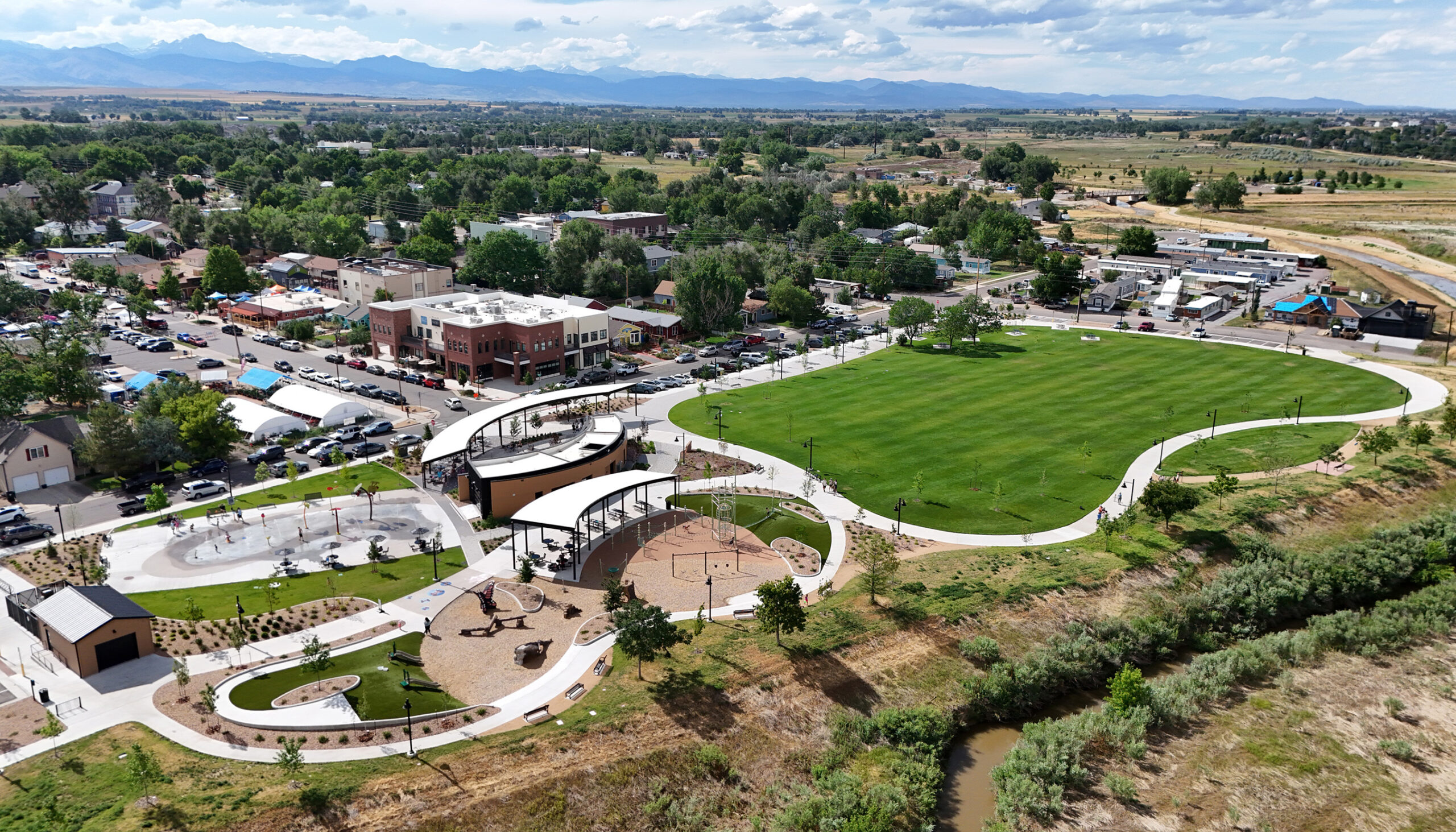 drone shot of Coal Creek Park shows the expansive green lawn, pavilion, splash pad, and playgrounds with the mountains in the distance