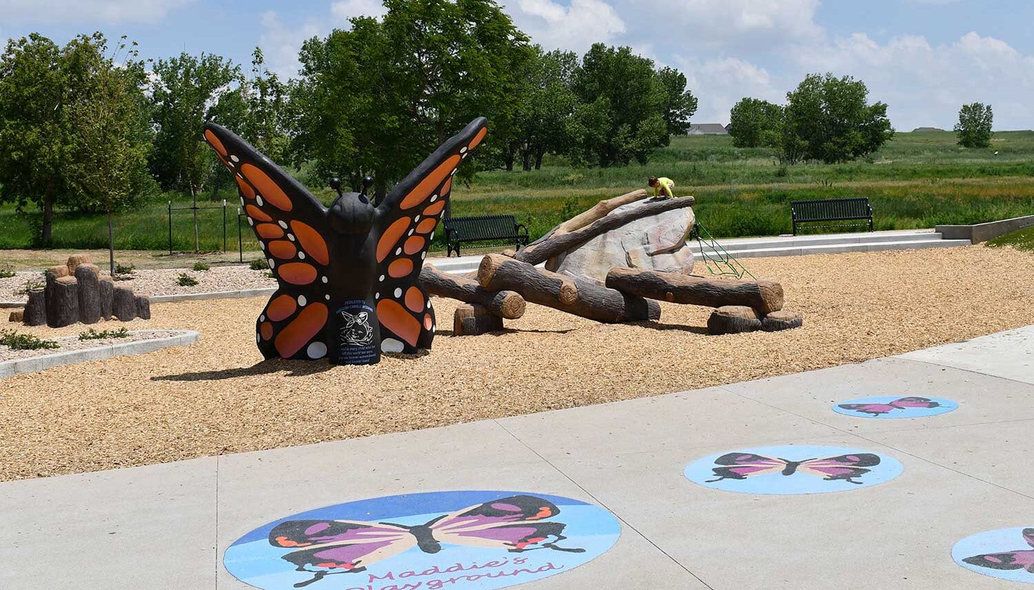 A large butterfly feature sits in the nature play area with grassland in the background.