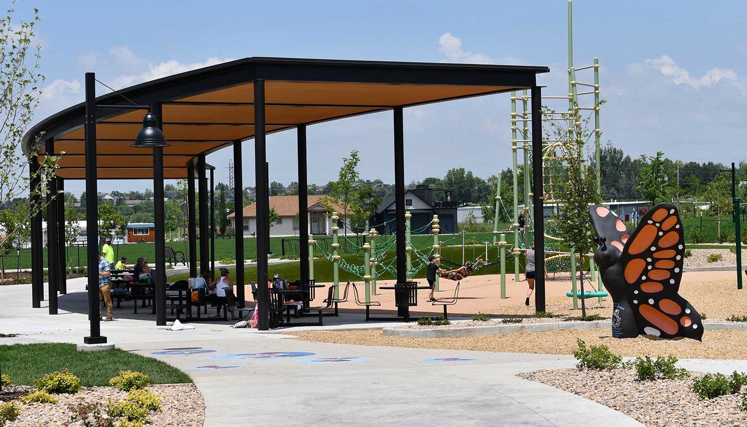A large pavilion shades people while kids play on the playground.