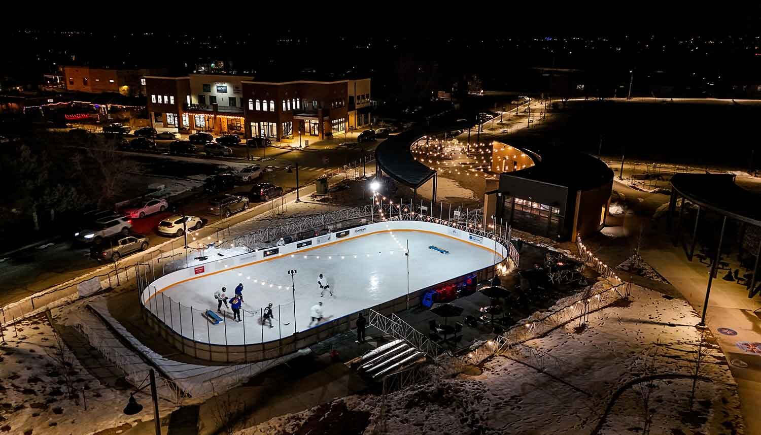A drone images at night of a lighted ice rink with hockey players.