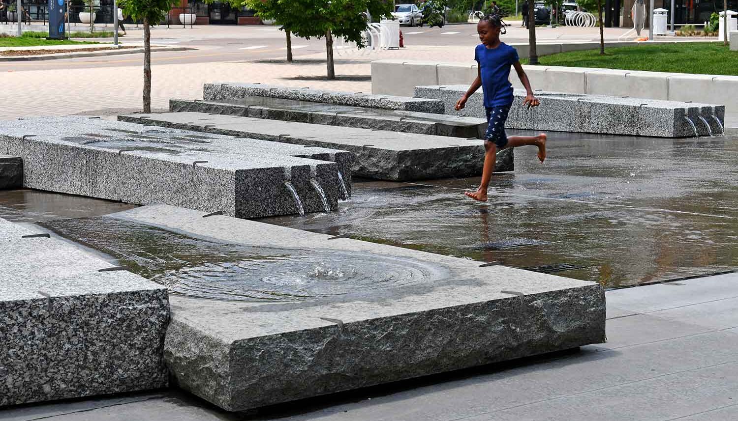Girl splashes through a granite stone water feature in the middle of the downtown plaza