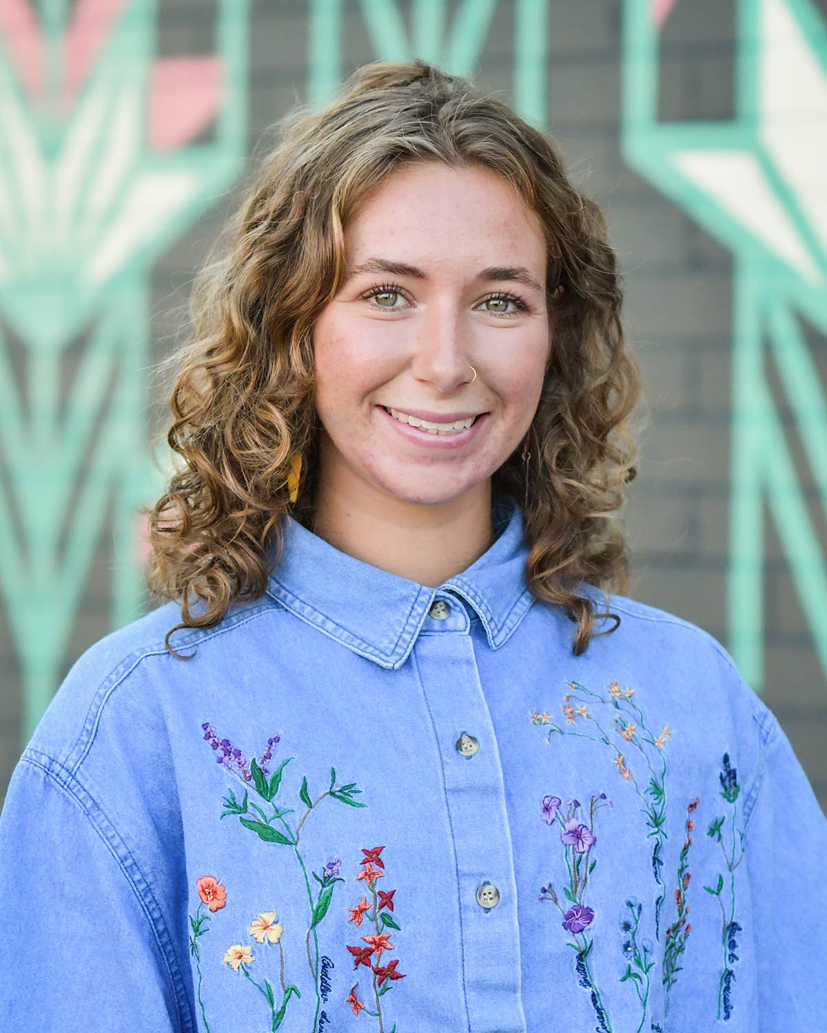 Headshot of Sarah in a blue denim shirt with embroidered flowers