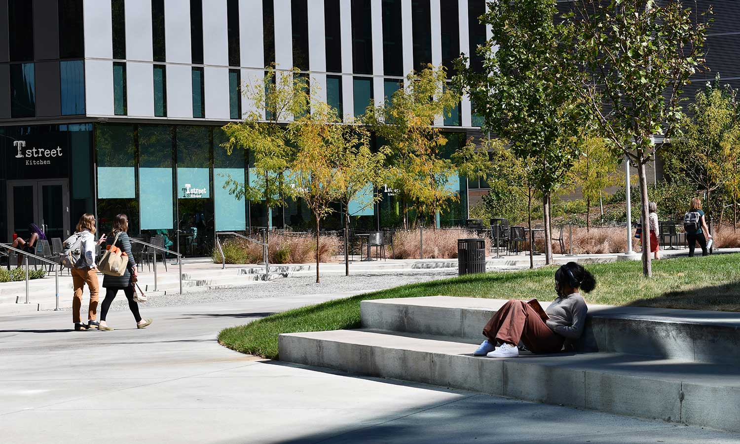 A student reads a book on the a seatwall along the campus Artwalk promenade.